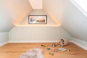 Ein Kinderzimmer mit schrägen Wänden, Holzboden, einem weichen Teppich und Spielzeug, das auf dem Boden verstreut liegt.