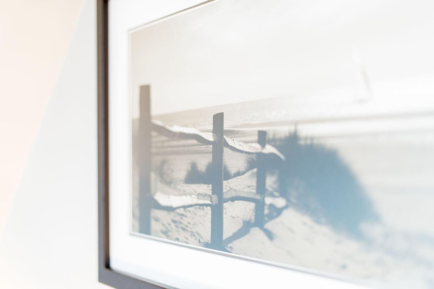 A framed photograph of a snowy landscape with a fence and trees.