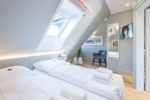 Un dormitorio moderno con tragaluces, una cama con ropa de cama blanca, un escritorio y una silla.