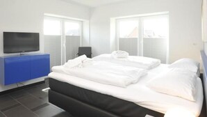 Una camera d'albergo moderna con un letto grande, una TV a schermo piatto, un mobiletto blu e ampie finestre.