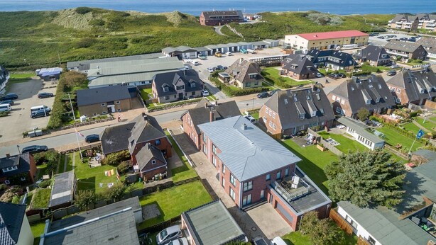 Vista aerea di una zona residenziale con case, un parcheggio e un edificio di grandi dimensioni con tetto rosso.