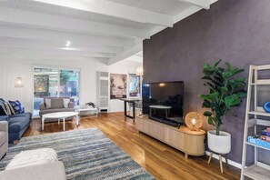 A modern living room with a flat-screen TV, a sofa, a coffee table, and a large plant.