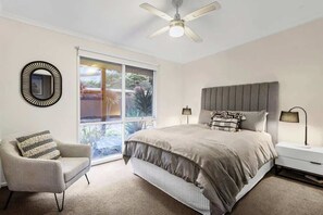 A bedroom with a bed, a chair, a nightstand, a lamp, and a ceiling fan.