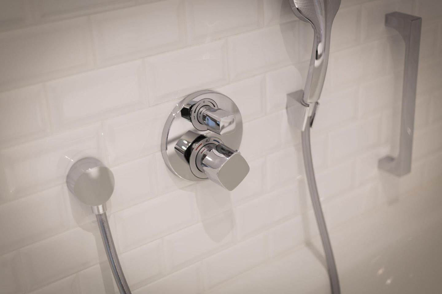 A modern bathroom with a chrome shower control panel, a handheld showerhead, and a wall-mounted faucet.