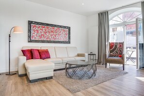 Ein modernes Wohnzimmer mit einem weißen Sofa, roten Kissen, einem Couchtisch und einem großen Fenster mit Vorhängen.