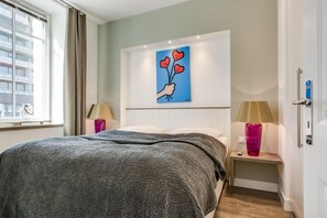 Camera d'albergo con un letto, due comodini con lampade, una finestra con tende e un quadro appeso al muro.