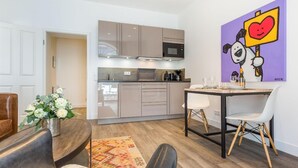 Una cuina moderna amb electrodomèstics integrats, zona de dinar amb taula i caires, i una obra d'art colorida a la paret.