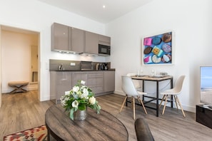 Eine moderne Küche mit grauen Schränken, ein Essbereich mit einem Holztisch und weißen Stühlen sowie ein farbenfrohes Kunstwerk an der Wand.