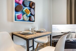 Un espace repas moderne avec une table en bois, des chaises blanches et un grand tableau encadré représentant des chocolats.