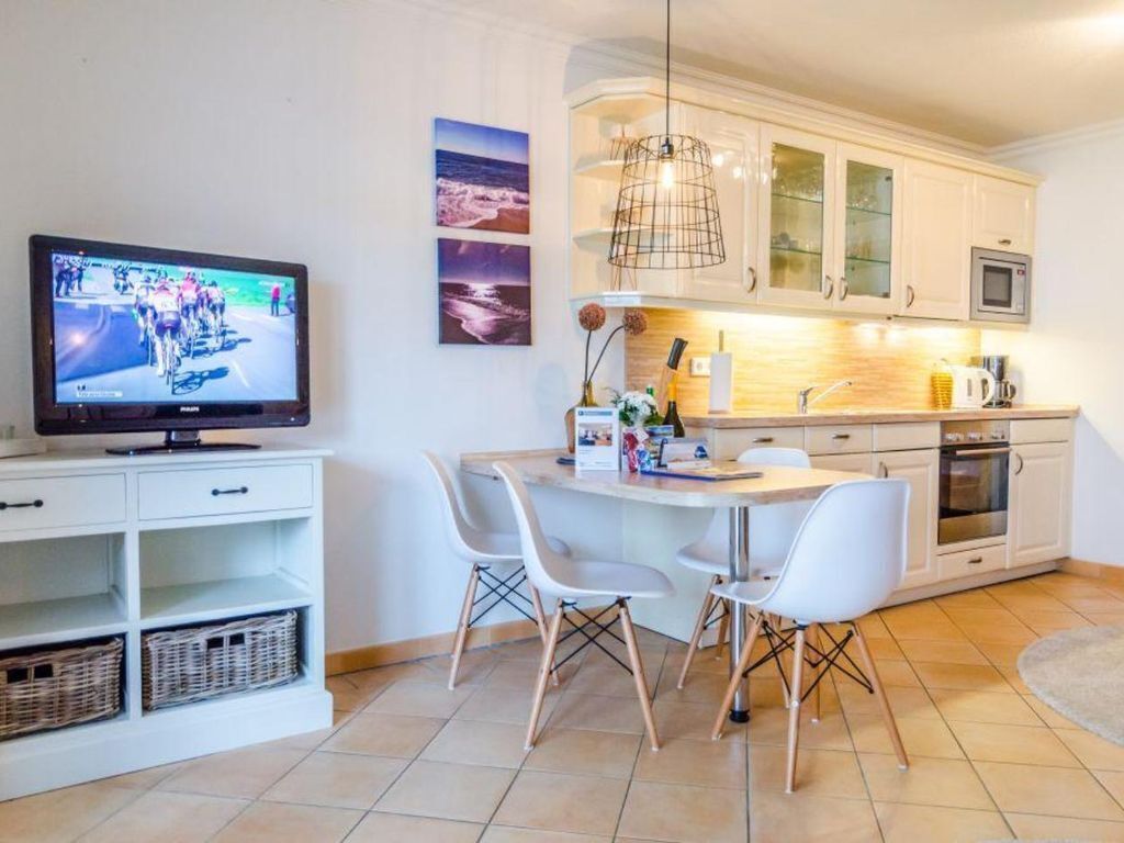 Een moderne keuken met witte kastjes, een magnetron, en een eethoek met witte stoelen.