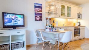A modern kitchen with white cabinets, a microwave, and a dining area with white chairs. - Residence Bismarck, Whg. 5a - Residence Bismarck (Sylt)