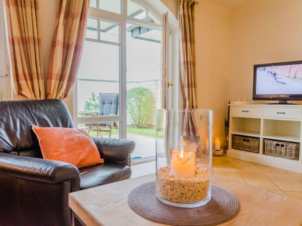 Een woonkamer met een leren bank, een glazen kandelaar met een brandende kaars, een televisie en uitzicht op het omliggende landschap door grote ramen.