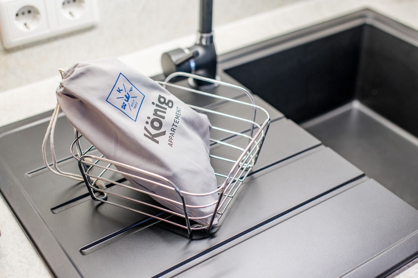Una cocina con un lavamanos, una estantería metálica y una bolsa con el nombre "König".