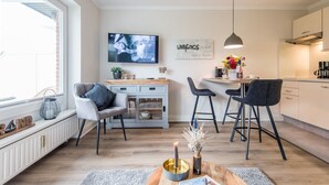 Een moderne keuken met een eethoek, een aan de muur bevestigde televisie, en een bord met de tekst 'LIEB KINGS Platz'.