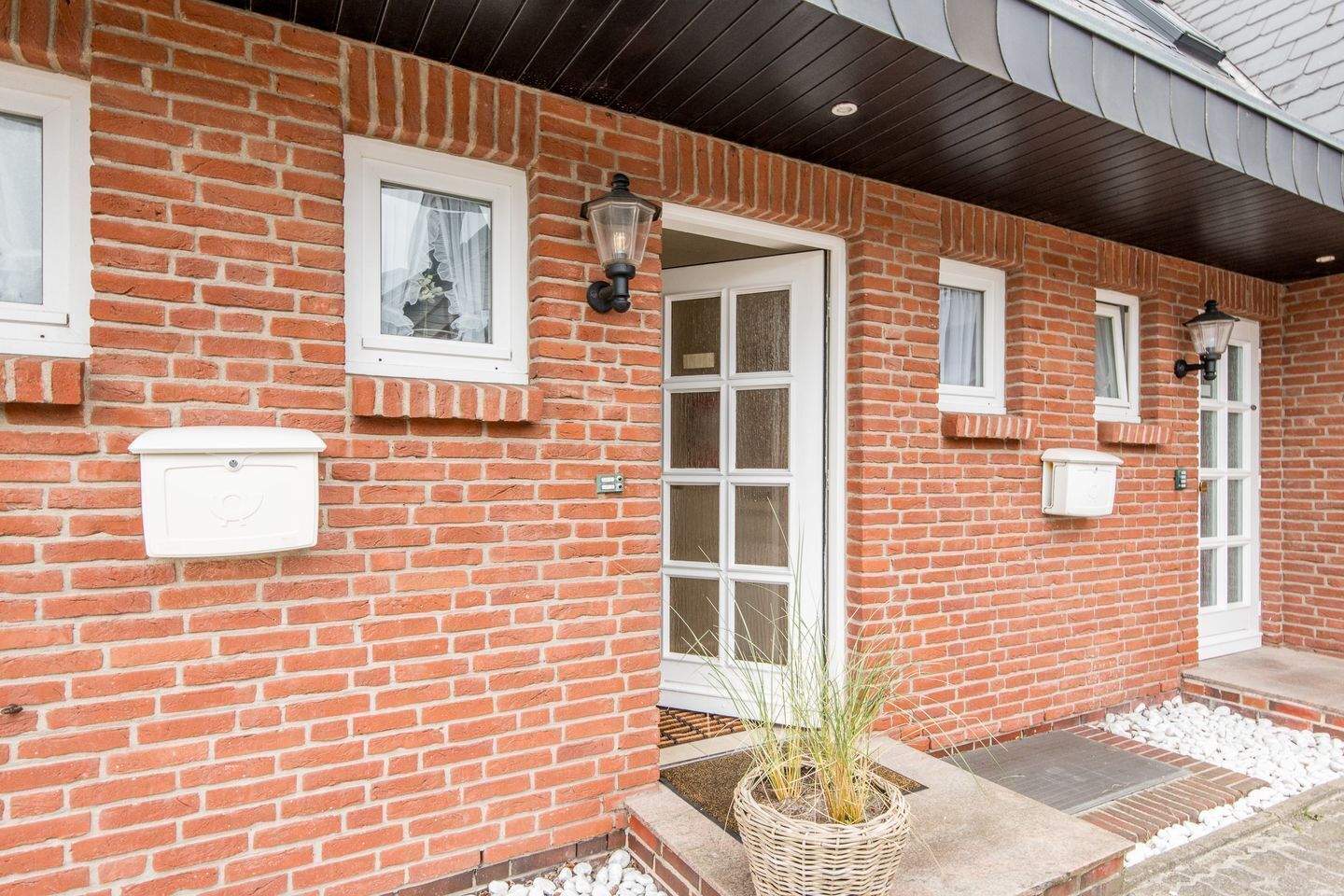 Un bâtiment en briques avec des fenêtres à cadre blanc, une porte et deux luminaires fixés au mur.