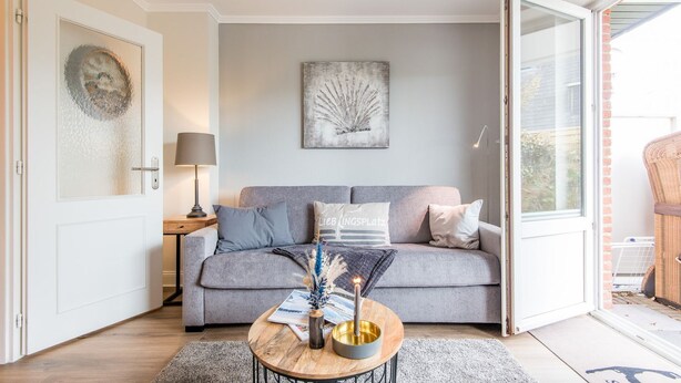 Een moderne woonkamer met een grijze bank, een ronde houten salontafel en een schilderij aan de muur.