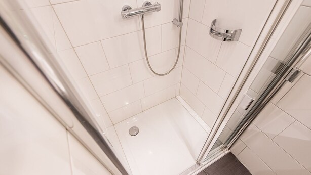 Een moderne douche met een glazen deur, chroombeslag en witte betegelde wanden.