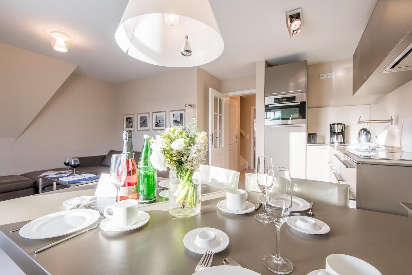 A modern dining area with a table set for four, a kitchen in the background, and a living area with a sofa and a coffee table.