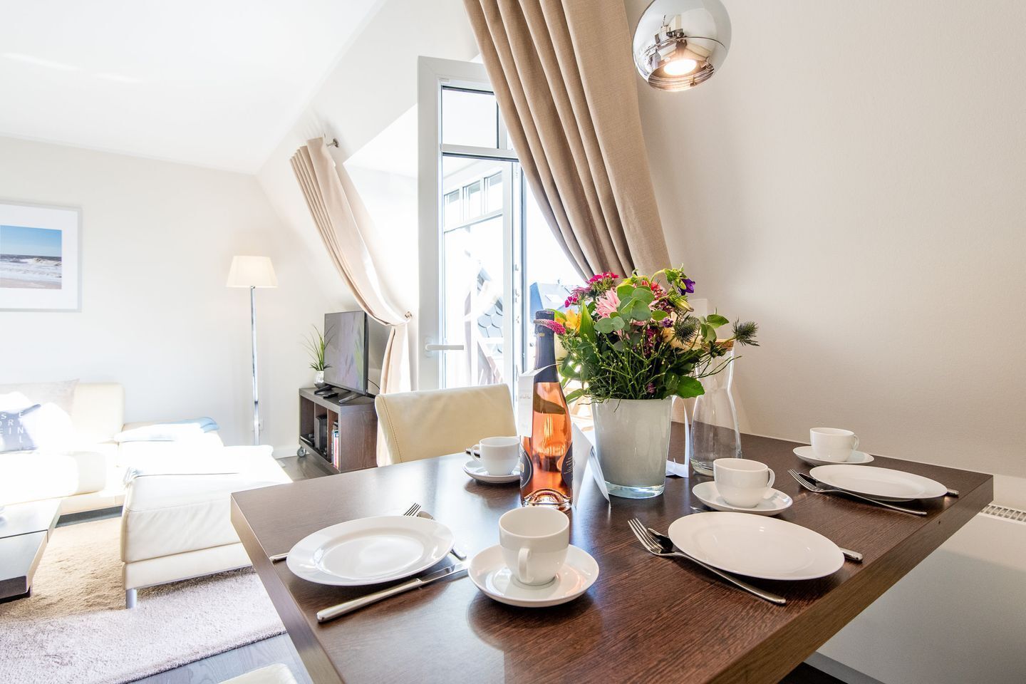 Ein Essbereich mit Tisch für zwei, einem Blumenstrauß und einer modernen Lampe.