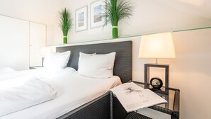 A hotel room with a bed, a nightstand with a lamp, and two green plants on the headboard. - House Nordmarkgarten, Whg. 7 - House Nordmarkgarten (Sylt)