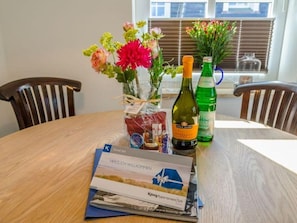 Een ronde houten tafel met een brochure, een fles wijn, een glas water en een bloevas.