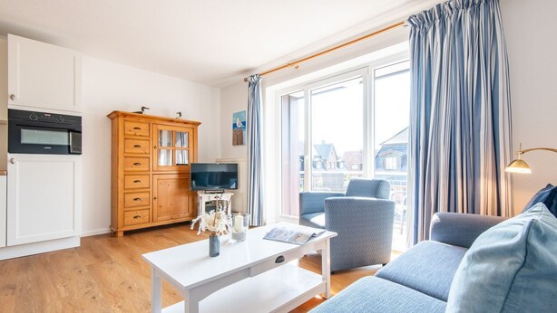 A modern living room with a sofa, a coffee table, and a TV. There's a wooden cabinet and a window with curtains. - House Hauke, Whg. 6 - House Hauke (Sylt)