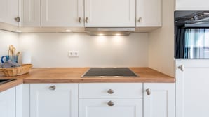 A modern kitchen with white cabinets, a wooden countertop, a built-in oven, and a window with curtains. - House Hauke, Whg. 6 - House Hauke (Sylt)