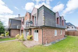 Ein zweistöckiges Backsteinhhaus mit Balkon, kleinem Garten und gepflasterter Auffahrt.