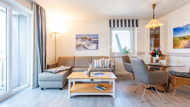 A modern living room with a sofa, coffee table, and dining area, large windows, and artwork on the walls. - House Hauke, Whg. 8 - House Hauke (Sylt)
