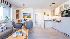 A modern kitchen with white cabinets, a dining area with a wooden table, and a living room with a sofa and chairs. - House Hauke, Whg. 8 - House Hauke (Sylt)
