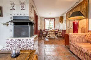 Un salon chaleureux avec une cheminée, un coin repas avec une table et des chaises, et un canapé agrémenté d’un coussin à rayures.