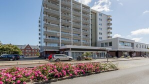 Un hotel moderno a più piani, con balconi su ogni piano, un'area parcheggio e un giardino curato con fiori rosa.