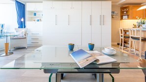 Een moderne keuken met witte kasten, een glazen eettafel en een blauwe stoel.