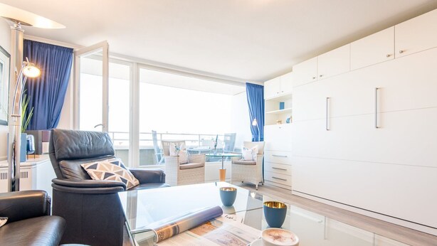 Een moderne hotelkamer met een leren bank, een glazen salontafel, een zithoek met rieten stoelen en een groot raam met uitzicht.