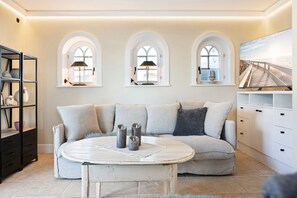 A cozy living room with a beige sofa, a round coffee table, and three arched windows with lamps.
