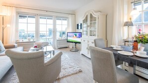 Un soggiorno moderno con TV a schermo piatto, un'area pranzo con tavolo apparecchiato per due e un ampio mobile bianco con ante in vetro.