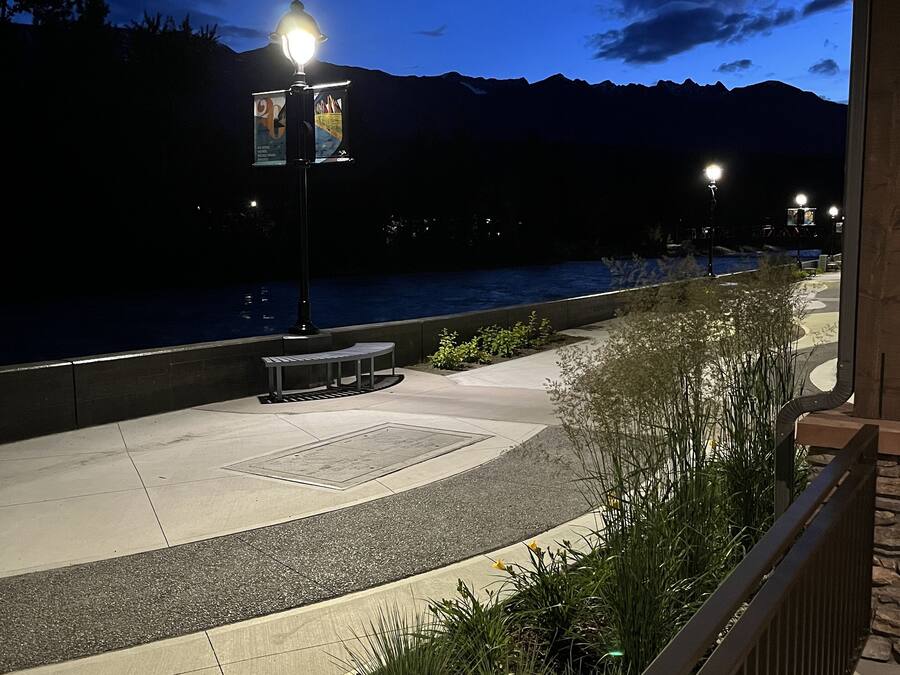 A waterfront promenade at dusk with street lamps, benches, and a view of the water.