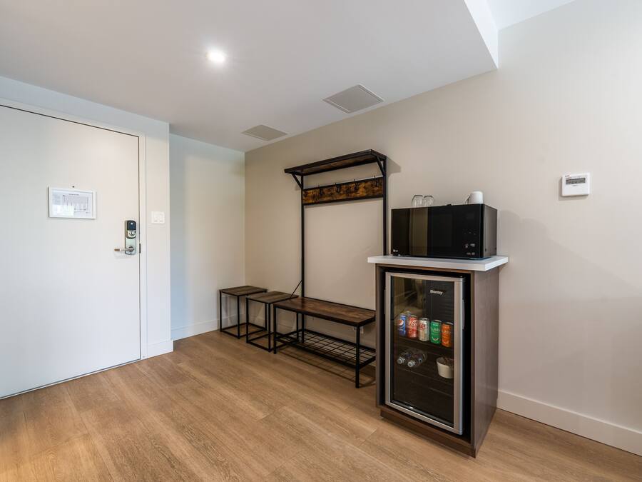 A room with a white door, a small table, a microwave on a cabinet, and a thermostat on the wall.