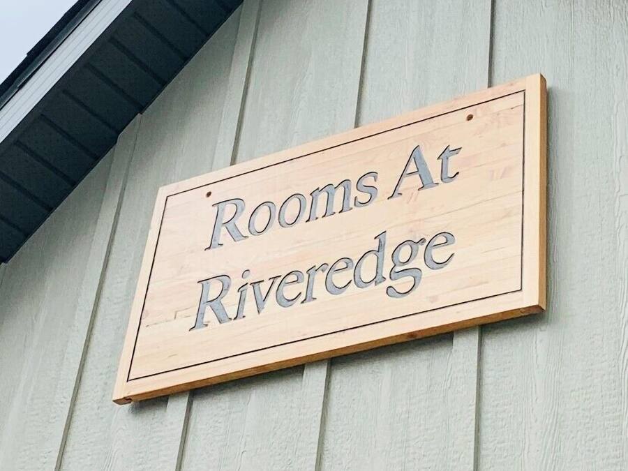A wooden sign on a building that reads "Rooms At Riveredge."