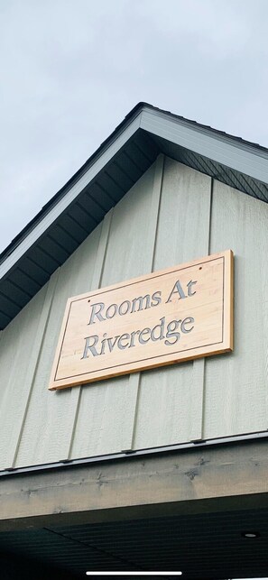 A wooden sign on a building that reads "Rooms At Riveredge."