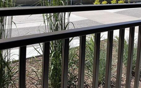 A view from a balcony with a railing, featuring a street with trees and a mountain range in the background.