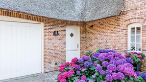 A brick building with a white garage door and a door with a black bell. - Twesk Diker 3, Germany (Sylt-Ost)