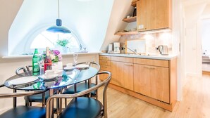 A modern kitchen with wooden cabinets, a dining table with chairs, and a large window providing natural light. - Twesk Diker 3, Germany (Sylt-Ost)