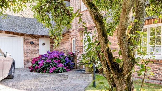 A brick house with a garage, a driveway, and a tree in the foreground. - Twesk Diker 3, Germany (Sylt-Ost)
