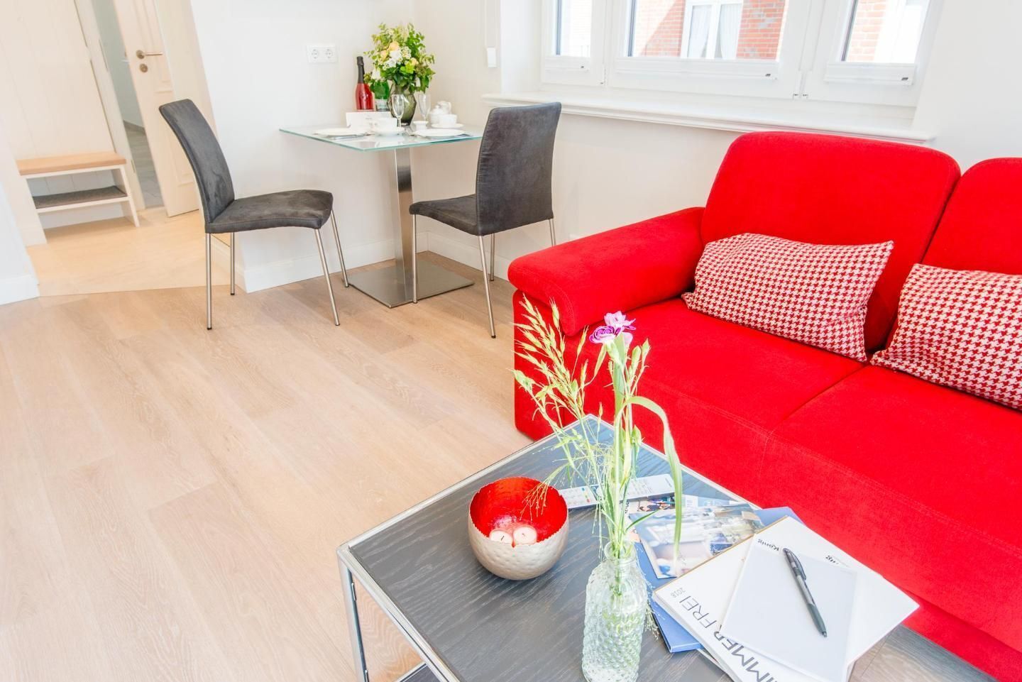 Una sala de estar moderna con un sofá rojo, dos sillas negras, una mesa de vidrio y una mesita de centro con un florero y un tazón.