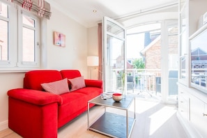 A bright living room with a red sofa, a glass coffee table, and a view of the outside. - House Mateika, Whg. 10 Sammy - House Mateika (Sylt)