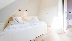 Ein Schlafzimmer mit schräger Decke, weißer Bettwäsche und Blick auf ein Badezimmer durch eine geöffnete Tür.