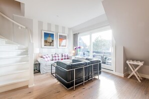 Una sala de estar moderna con una escalera, un conjunto de sofás y un gran ventanal con vistas al exterior.