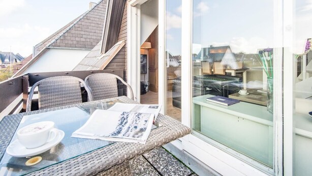 Ein Balkon mit Korbmöbeln, einem Glastisch und einer Kaffeetasse.