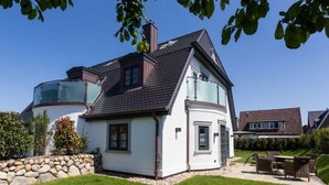 Une maison à deux étages avec un mur en pierre, un balcon et une pelouse bien entretenue.